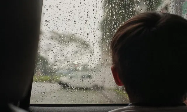 Dziecko patrzy przez zaparowane kroplami deszczu okno, szukając pomysłów na zabawy na deszczowe dni.