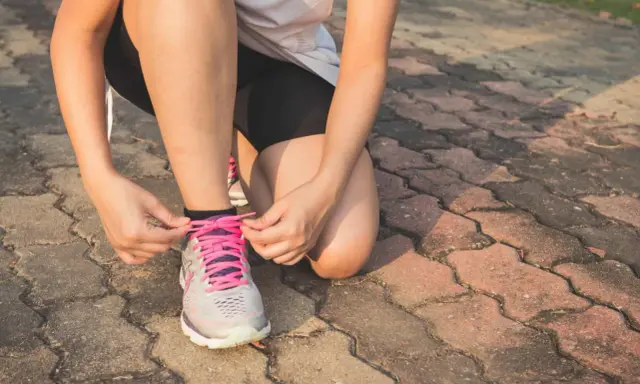 Kobieta w sportowym stroju klęczy i zawiązuje sznurówki w butach do **slow joggingu**.
