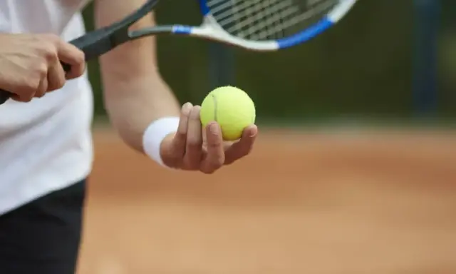Gracz trzyma piłkę tenisową, gotowy do serwisu. Kluczowy moment decydującego **tenis tie break**.