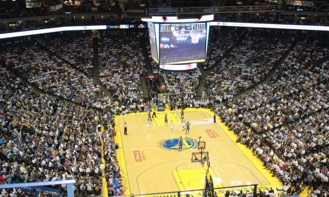Mecz koszykówki w Oracle Arena. Na boisku gracze, na trybunach tłumy kibiców. Na telebimie widać wynik, który sugeruje, że gra jest w końcowej fazie, być może ostatni z czterech kwart.