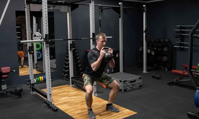 Mężczyzna wykonuje przysiad z kettlebell trzymanym w chwycie nachwyt i podchwyt.