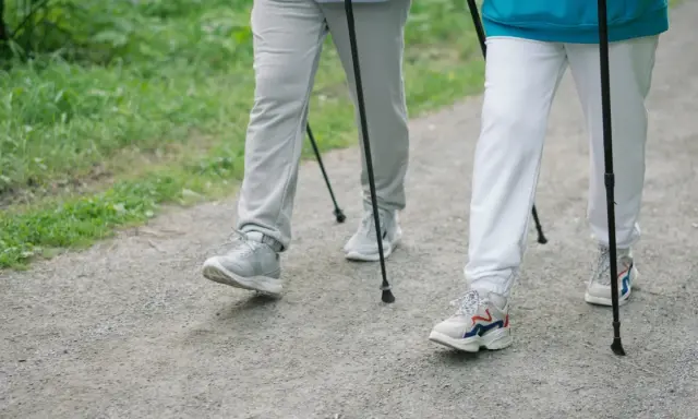 Dwie osoby idące z kijkami po leśnej ścieżce. Pokazują, jak chodzić z kijkami, czerpiąc radość z aktywności na świeżym powietrzu.