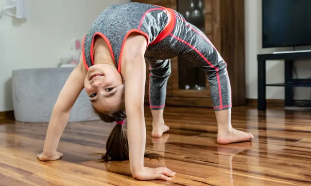 Uśmiechnięta dziewczynka w sportowym stroju wykonuje mostek. To świetna gimnastyka dla dzieci, rozwijająca gibkość i siłę.