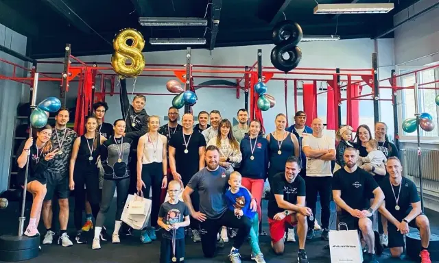 Uśmiechnięta grupa świętuje sukcesy na siłowni. Sportowe grupowe zdjęcie z medalami i balonami w kształcie ósemek.