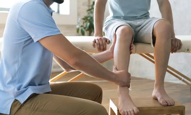 Fizjoterapeuta pomaga w domowej rehabilitacji stawu skokowego, delikatnie masując nogę pacjenta.