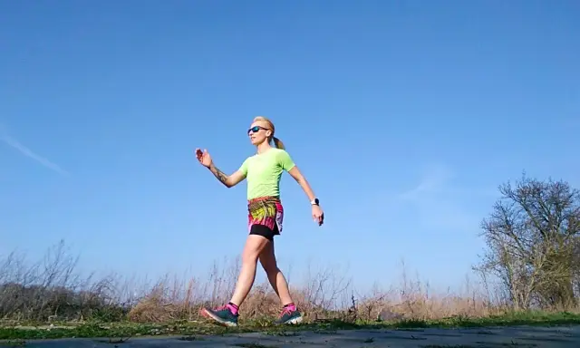 Kobieta w sportowym stroju ćwiczy marsz, stosując metodę Gallowaya. Słoneczny dzień sprzyja aktywności na świeżym powietrzu.