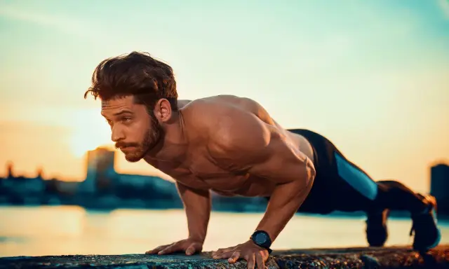 Mężczyzna wykonuje pompki na biceps przy wodzie o zachodzie słońca.