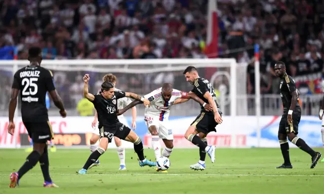 Piłkarze walczą o piłkę, przestrzegając zasad gry. W akcji widać zawodników w białych i czarnych strojach, zmagających się na zielonej murawie stadionu.