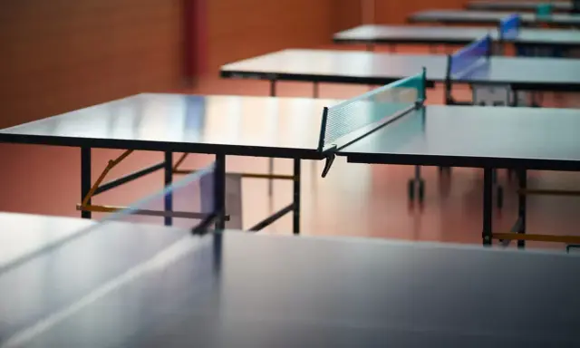 Rzędy stołów do ping ponga czekają na graczy. Sieć do ping ponga jest napięta, gotowa na emocjonującą grę.
