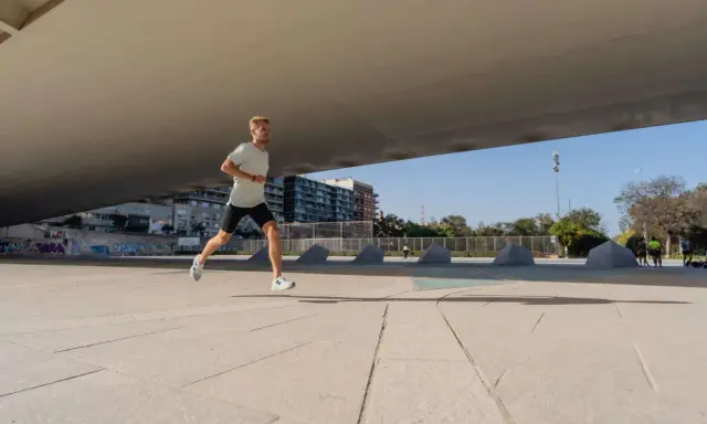 Mężczyzna w lekkim stroju sportowym biegnie po betonowym placu, przygotowując się do biegu na 10 km. W tle budynki i drzewa.