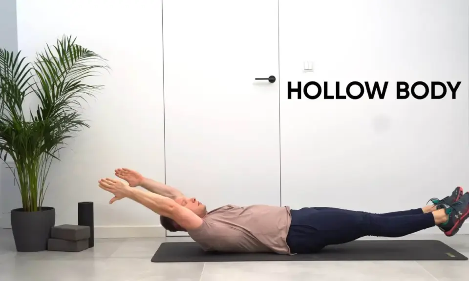 Mężczyzna ćwiczy pozycję hollow body na macie. Ręce wyciągnięte nad głowę, nogi uniesione.