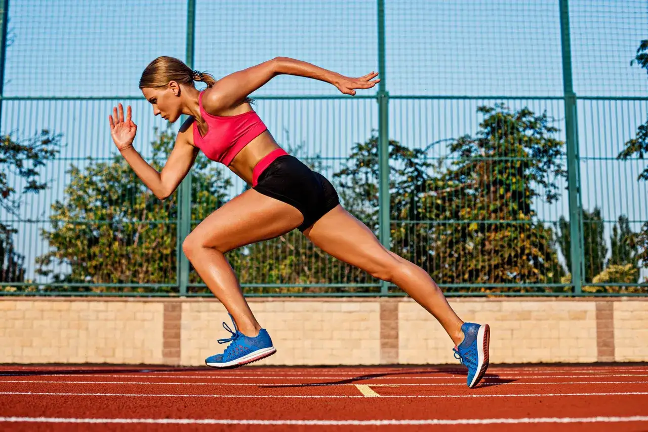 Kobieta w sportowym stroju wykonuje ćwiczenia na szybkość, dynamicznie biegnąc po bieżni.