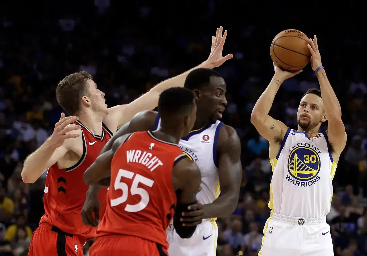 Stephen Curry, silny skrzydłowy, szykuje się do rzutu. Obrońcy próbują go zatrzymać.