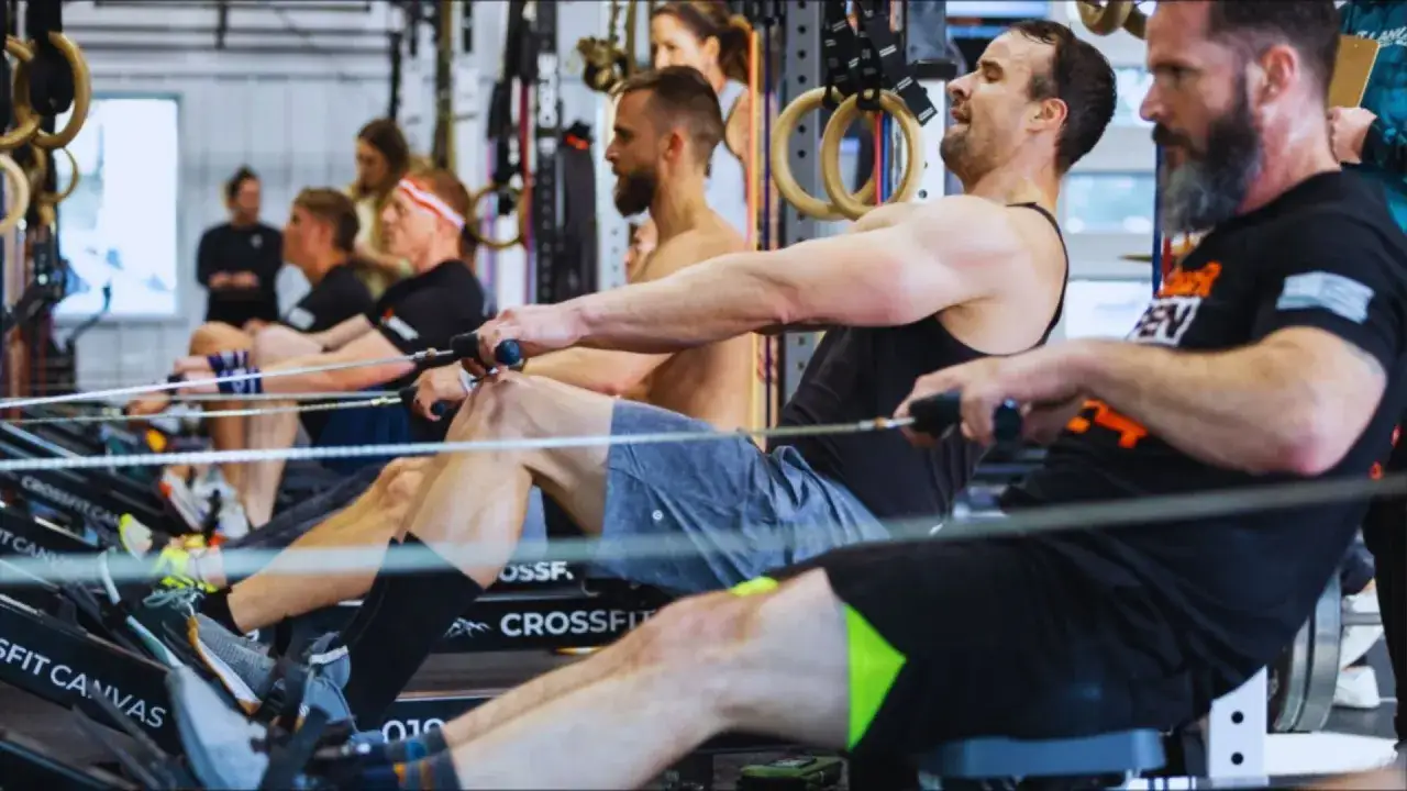 Mężczyźni trenują na wioślarzach w sali treningowej. To właśnie crossfit co to za trening, który buduje siłę i wytrzymałość.