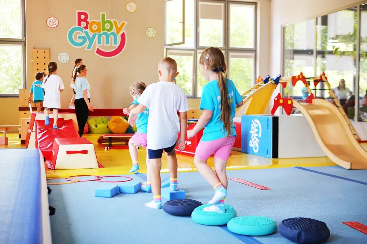 Dzieci ćwiczą na sali gimnastycznej Baby Gym, pokonując tor przeszkód. Radość i ruch to podstawa gimnastyki dla dzieci.