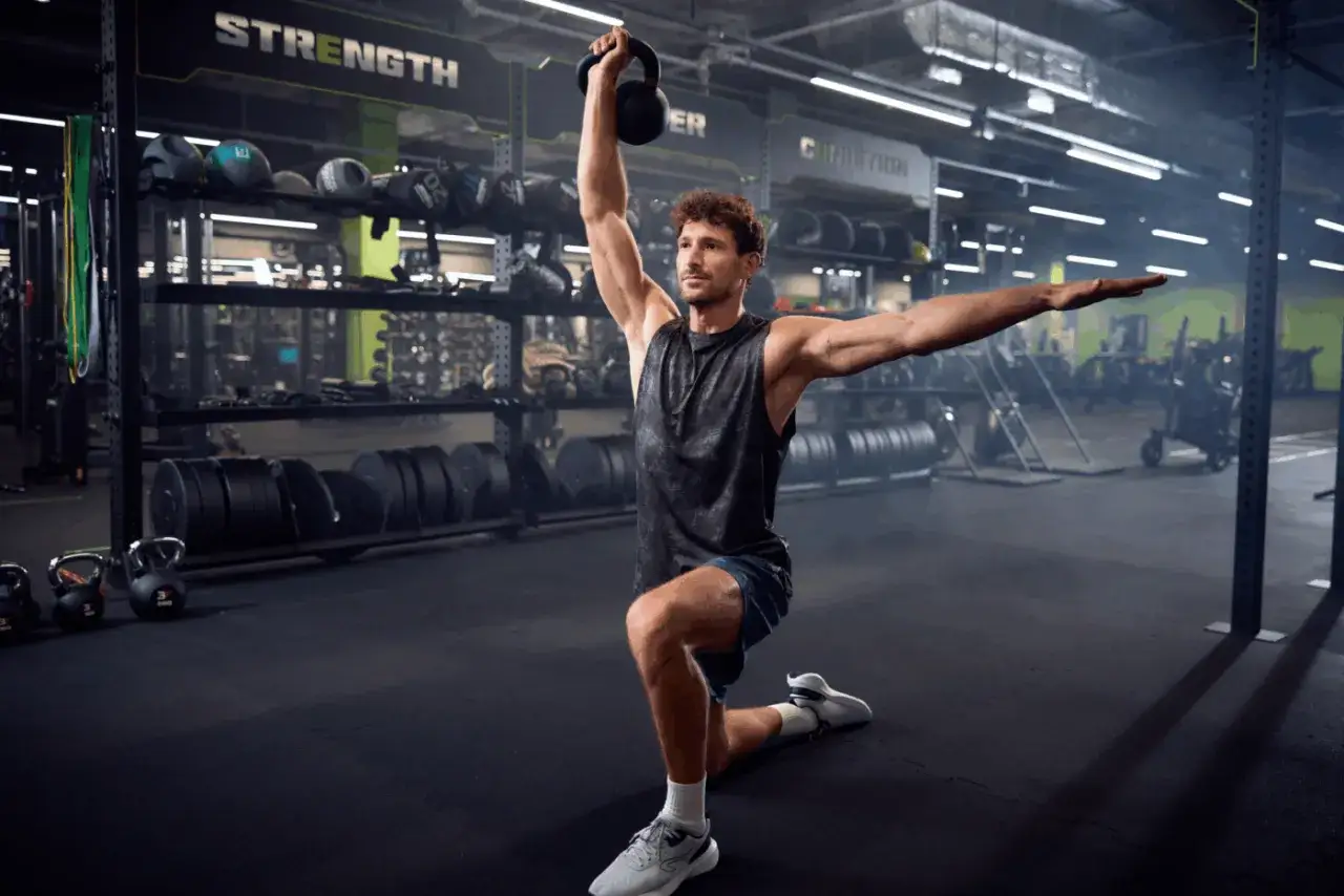 Mężczyzna wykonuje ćwiczenie z kettlebell w siłowni. TBC co to znaczy? To trening, który buduje siłę i wytrzymałość.