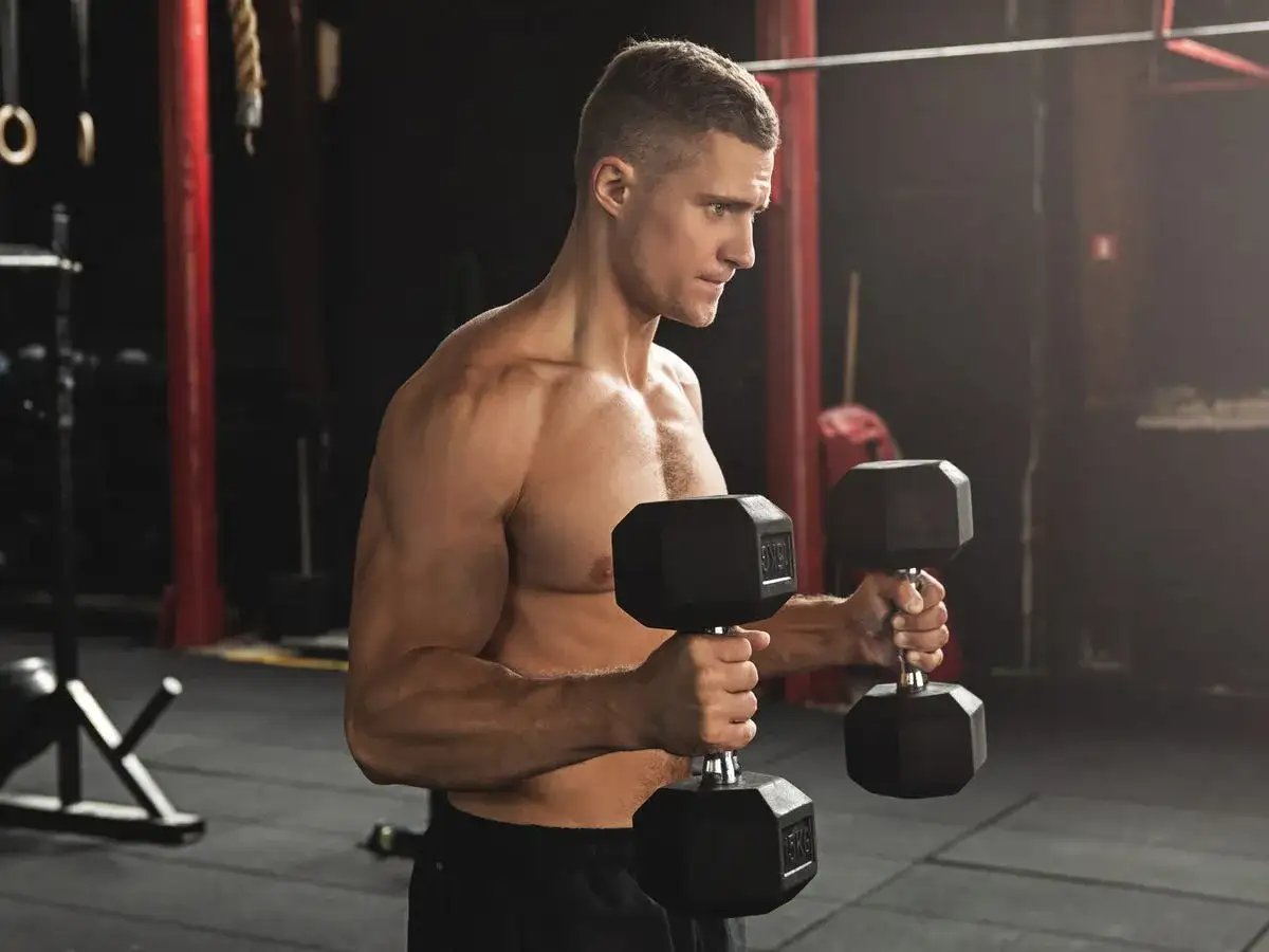 Mężczyzna z napiętym bicepsem trzyma ciężarki w siłowni, gotowy do treningu.