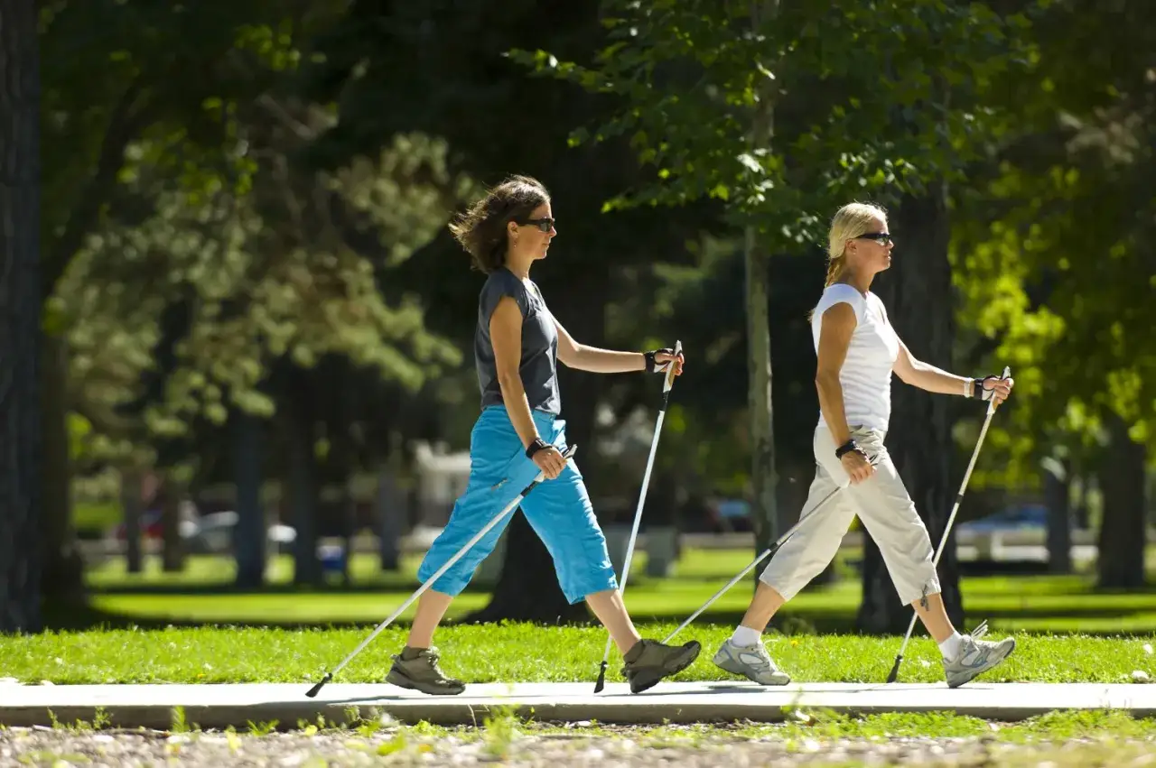 Dwie kobiety ćwiczą nordic walking w parku. Poprawna technika, jak chodzić z kijkami, zapewnia efektywny trening.