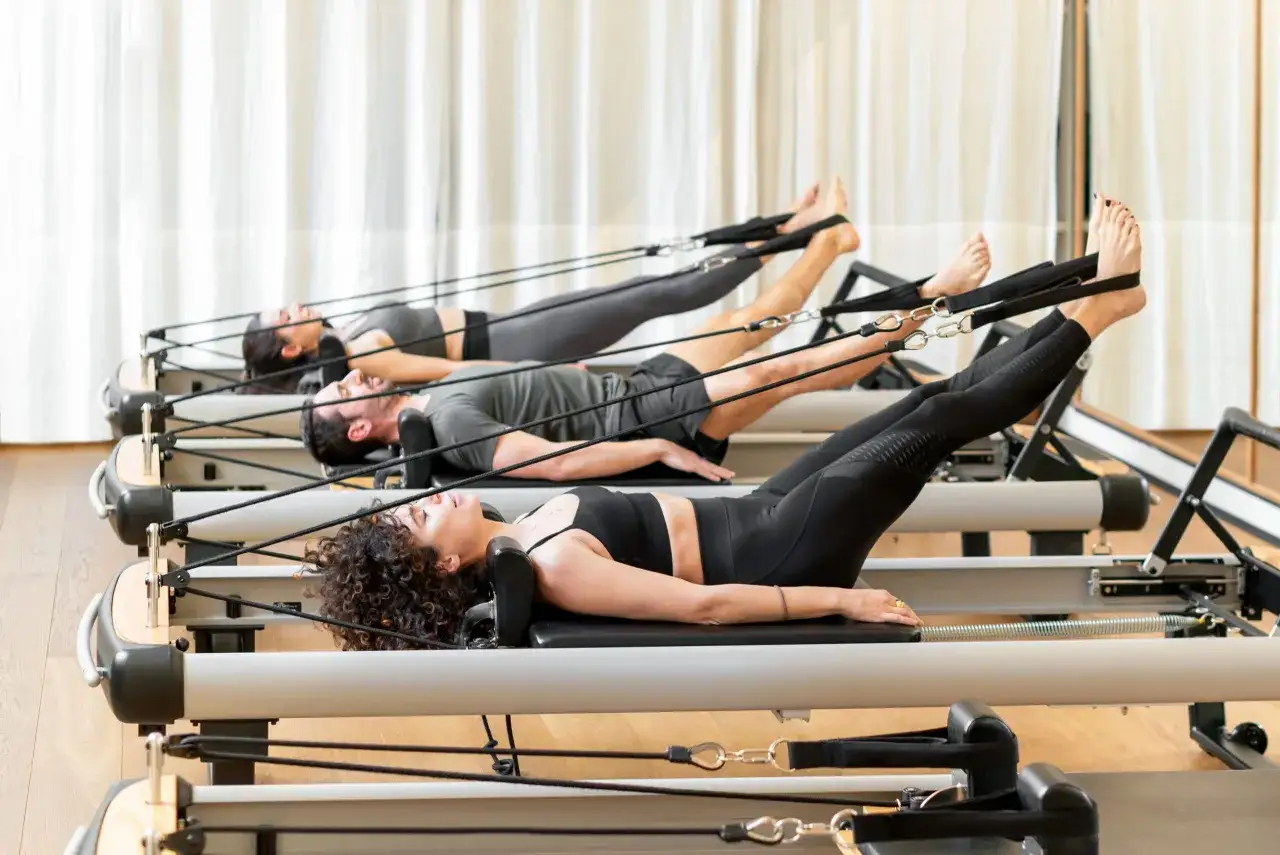 Trzy osoby ćwiczą pilates na reformerach. To świetny trening dla każdego, kto chce wzmocnić ciało i poprawić elastyczność.
