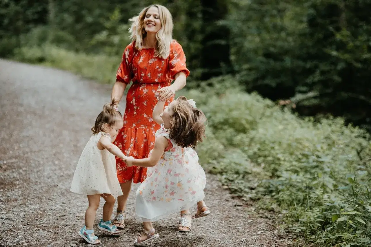 Mama z córkami tańczy na leśnej ścieżce. Radosne zabawy rytmiczne dla dzieci na łonie natury.