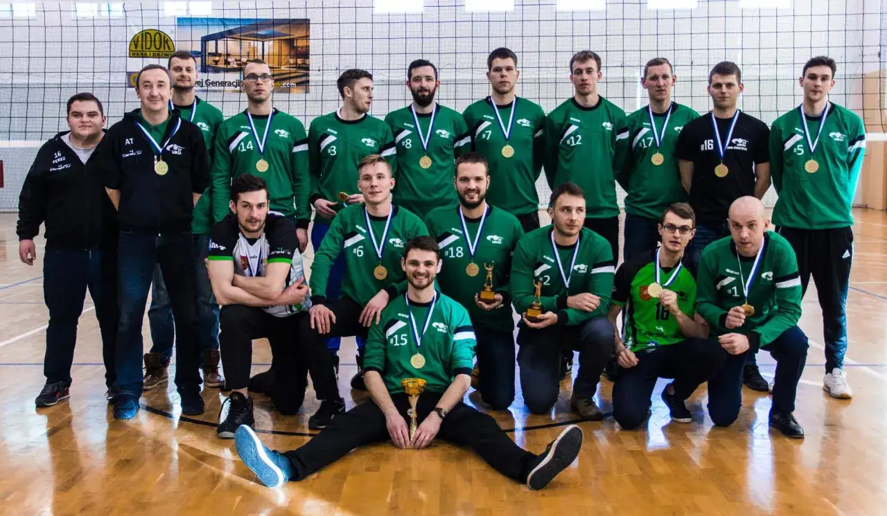 Drużyna siatkarzy świętuje sukces, pozując do zdjęcia z medalami i pucharami. To piękny moment w ich historii siatkówki.