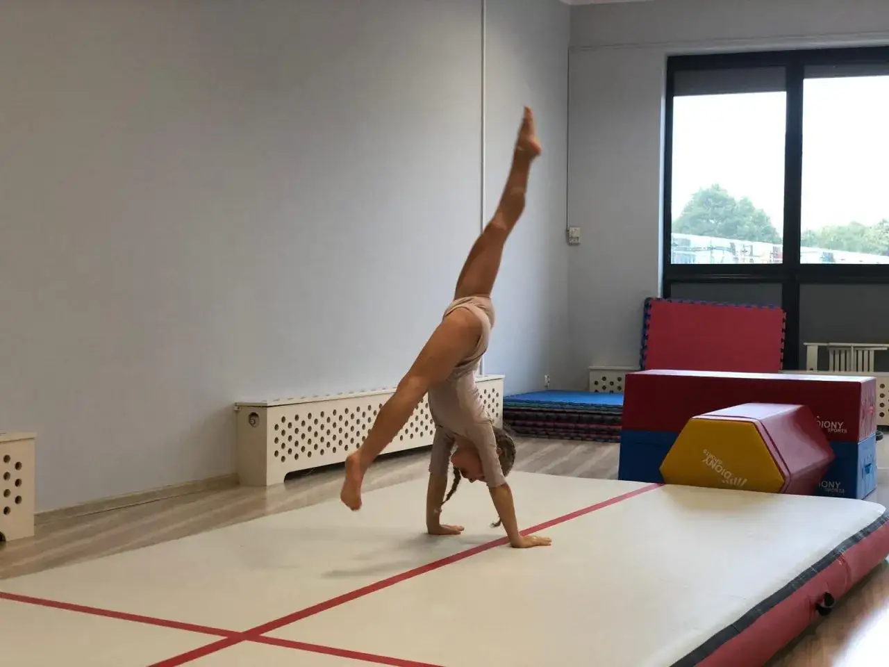 Młoda gimnastyczka wykonuje stanie na rękach podczas zajęć sportowych dla młodzieży.