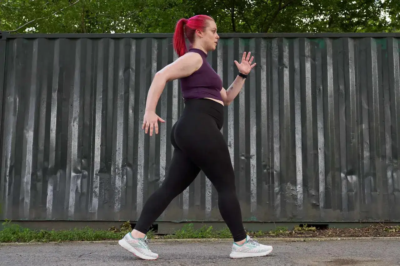 Kobieta z r&oacute;żowymi włosami w kucyku uprawia power walking w czarnych legginsach i sportowym topie.