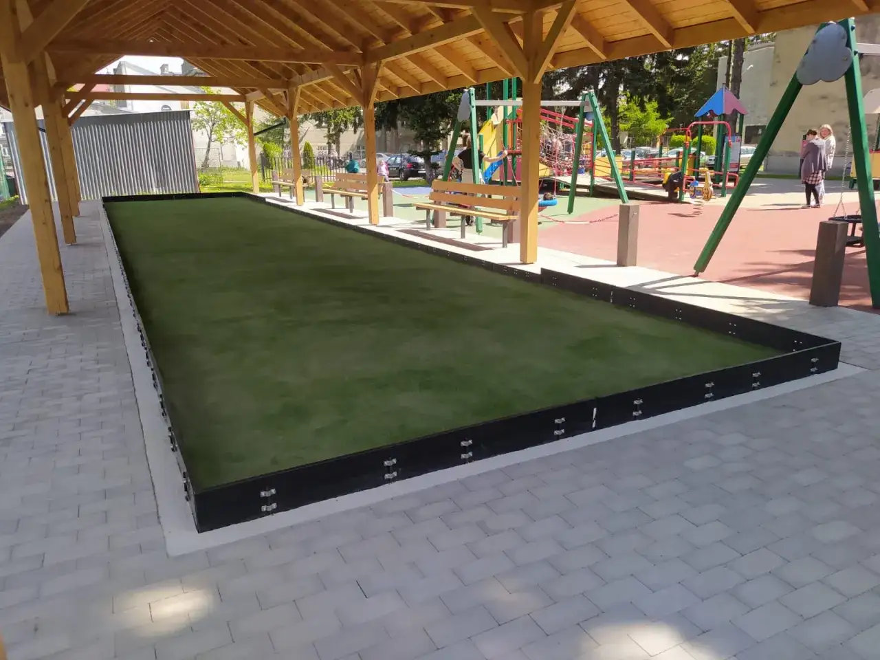 Boisko do gry w boccia, co to za sport? Sztuczna trawa, ławki i plac zabaw w tle.