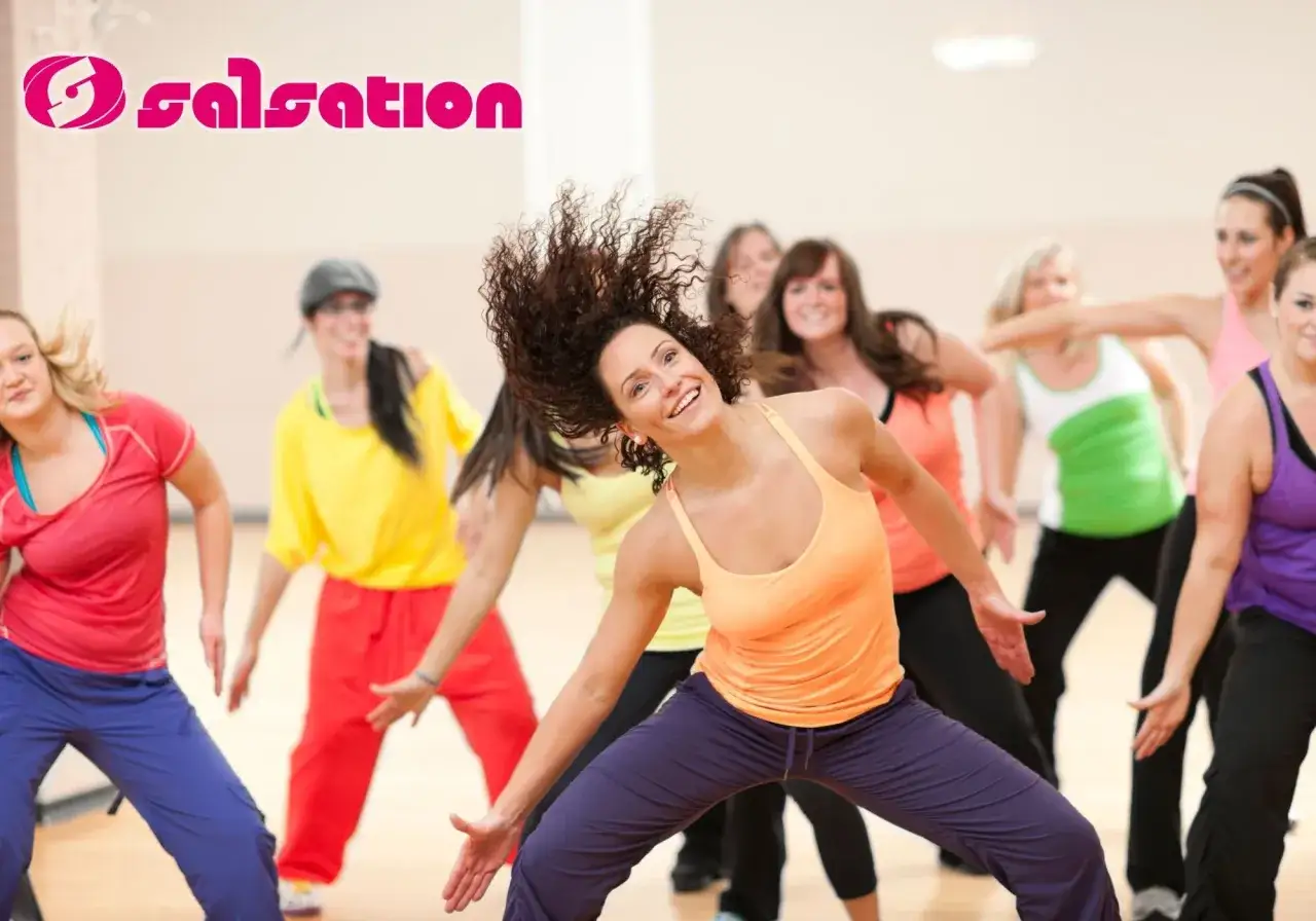 Grupa kobiet tańczy w rytm muzyki, uśmiechając się. To właśnie salsation – trening łączący taniec i fitness.