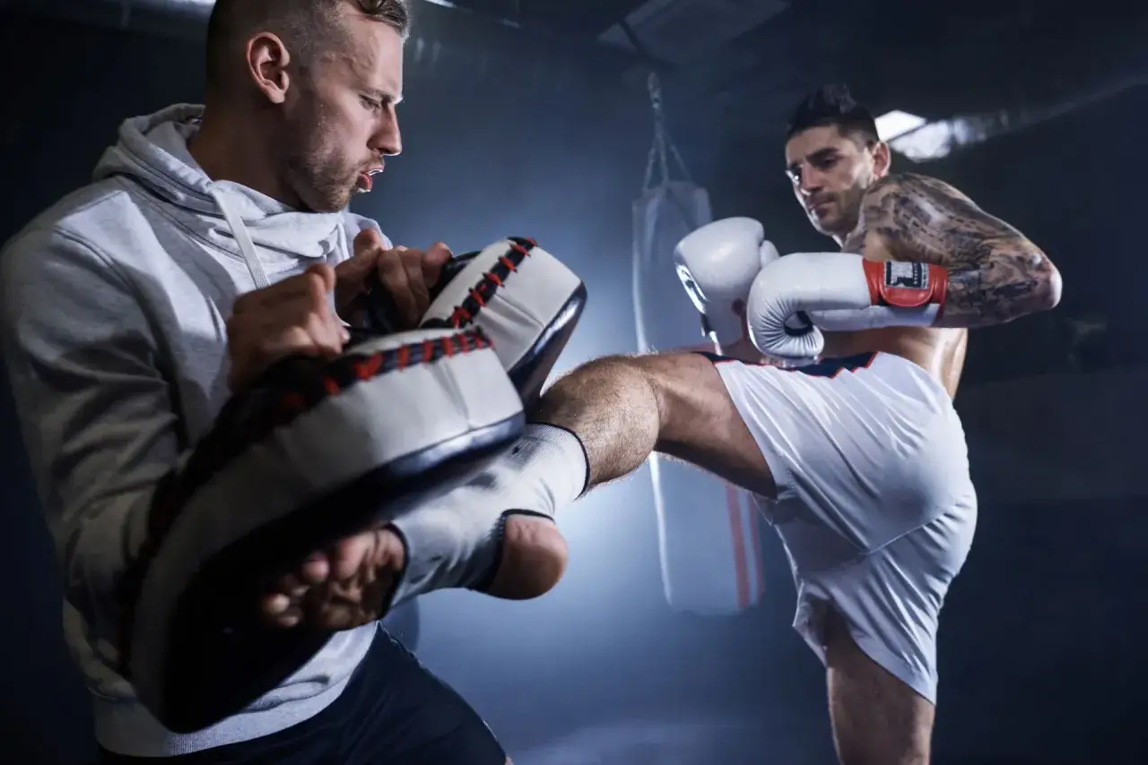 Intensywny trening muay thai i kickboxingu. Zawodnik wykonuje kopnięcie, a trener odbija je na łapach treningowych.