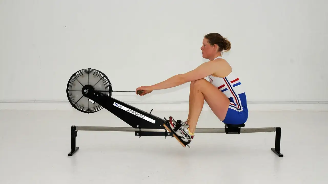 Kobieta w stroju sportowym wykonuje trening na wioślarzu. Jej plan treningowy zakłada intensywną pracę nad siłą i wytrzymałością.