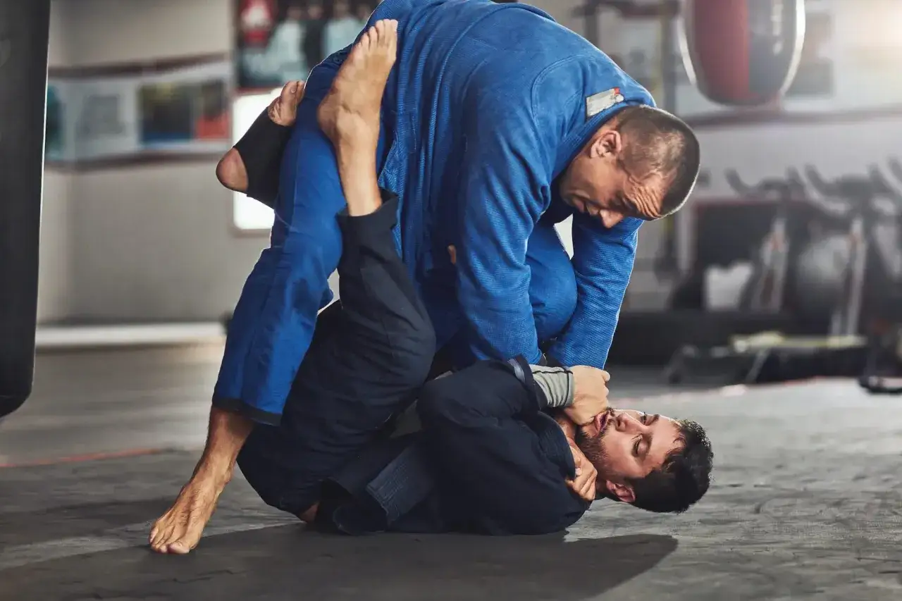 Intensywny trening BJJ. Dwóch mężczyzn w kimonach walczy na macie, jeden próbuje obalić drugiego.